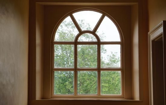 An elegant arched window design framing a lush green view of trees outside. Interior shot.