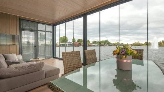 Elegant flowers bouquet placed on table with glass top in contemporary house with soft sofa and glass walls located on lake under overcast sky